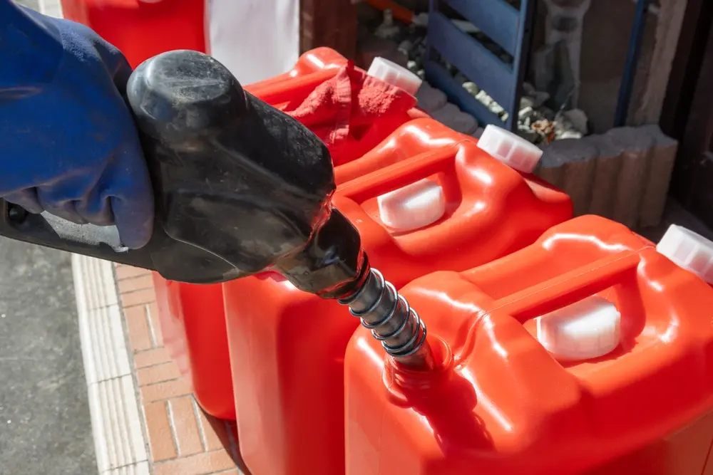 Person in blue gloves filling three orange containers with kerosene at Floyd Xpress Market